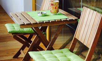A small table with two folding chairs is on a balcony. The furniture has green cushions and is made of wood.