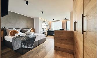 A modern bedroom with a large bed and elegant wood paneling. Large windows provide plenty of natural light and a beautiful view.