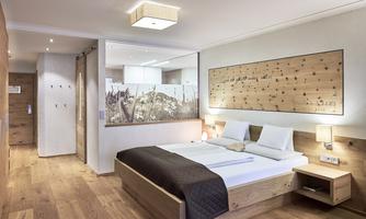 A modern bedroom with a large bed and warm wood elements. The wall is designed with a decorative wooden panel, and the room feels bright and inviting.