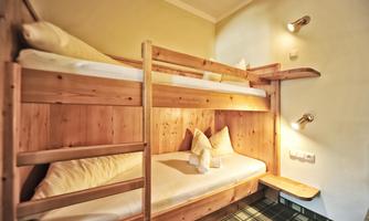 A cozy room with a wooden bunk bed. The walls are light, and the decor is simple and functional.
