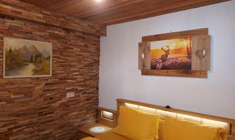 A cozy bedroom with wooden walls and a large bed with yellow pillows. Pictures of landscapes and a deer hang on the wall.