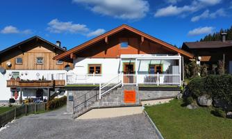 A modern house with an orange roof and a white extension. In the background, there are additional traditional buildings and blue sky visible.