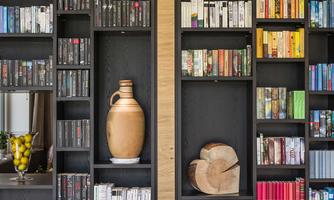 A modern bookshelf with various rows of books in different colors. On the left side, there is a decorative vase and a bowl of lemons.