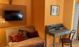 A cozy room with a sofa, a table, and a chair. The walls are painted in a warm orange, and a TV is mounted on the wall.