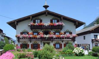 A traditional house with beautiful flower boxes and a green garden. The facade is friendly and inviting, surrounded by colorful flowers.