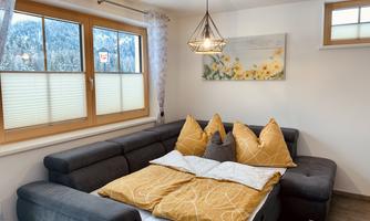 A cozy living room with a gray couch and orange cushions. In front of the window is a beautiful view of the mountains.