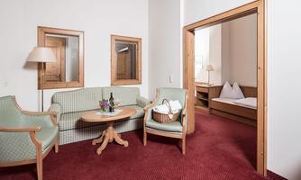 A cozy living space with a sofa, two armchairs, and a table. In the background, you can see a bedroom with two beds.