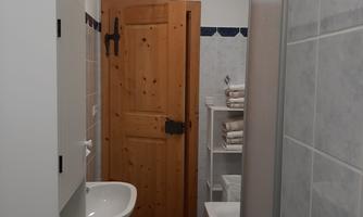 A modern bathroom with a shower, a sink, and a wooden window. The walls are light and the tiles are in a neutral color tone.