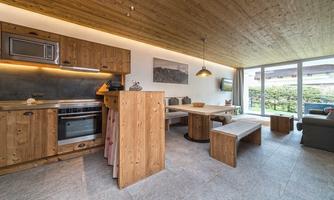A modern kitchen with wooden furniture and a dining area. Large windows let in plenty of light and offer a view of the outdoor area.