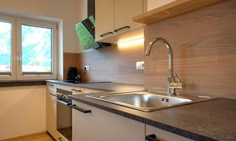 A modern kitchen with wooden elements and white furniture. The windows offer a view of the surrounding area.
