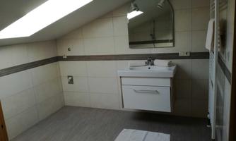 A modern bathroom with a sink and a large mirror. The room has bright tiles and a skylight that lets in daylight.