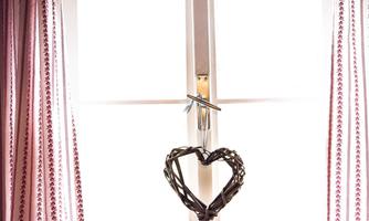 A window with white curtains and a heart-shaped decorative element made of twigs. The light gently flows into the room.