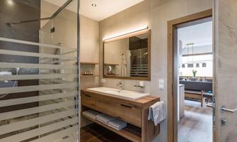 A modern bathroom with a comfortable shower and a wooden vanity. The walls are in neutral tones, and the lighting creates a pleasant atmosphere.