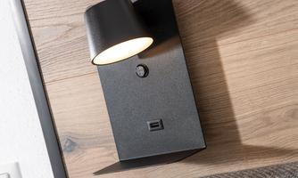 A modern wall lamp in black with a swiveling lampshade. It has a switch and a USB port.