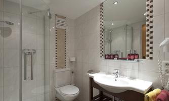 A modern bathroom with a shower and a sink. The walls are designed with light tiles, and the space feels clean and inviting.