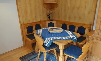A cozy dining area with a round table and wooden benches. The room has warm wood paneling and a blue carpet.