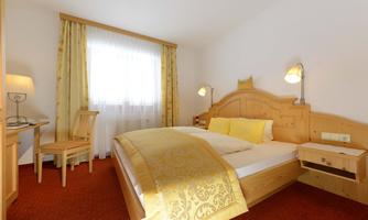 A cozy bedroom with wooden furniture and a large bed. The room has bright curtains and a warm atmosphere.