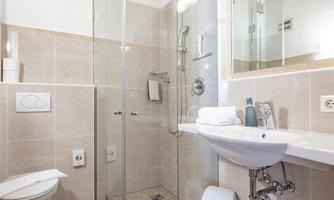 A modern bathroom with a glass shower cubicle and a sink. The walls are tiled in light colors, and a wooden ceiling provides a cozy atmosphere.