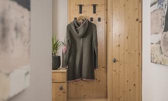 A cozy hallway with a wooden wall and a coat hanging on a hook. Next to it, there is a small plant in a pot.