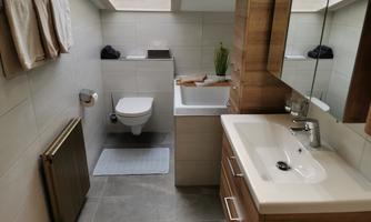 A modern bathroom with bright tiles and wooden details. There is a sink, a toilet, and some towels.