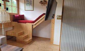 A cozy room with a wooden bed on a platform. A couch and a table complete the decor.