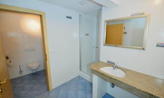 A modern bathroom with a shower, toilet, and sink. The walls are brightly tiled and the floor has a blue hue.