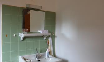 A simple bathroom with a white sink and a green tiled area. Towels are hanging on the wall and a mirror is present.