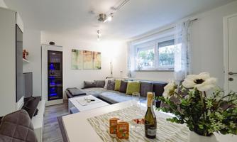 A modern furnished living and dining room with a cozy couch and a dining table. There are flowers, champagne, and snacks on the table.
