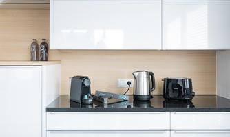 A modern kitchenette with bright cabinets. On the countertop, there is a kettle, a coffee machine, and a toaster.