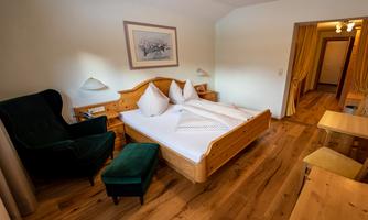A cozy hotel room with a double bed and wooden floor. There is an armchair, a small table, and warm lighting for a relaxing atmosphere.