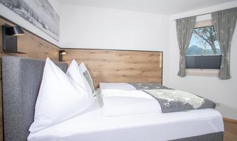 A modern bedroom with a comfortable bed and white pillows. The walls are bright and the window lets in a lot of daylight.