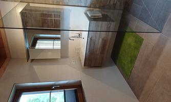 A modern bathroom with a glass shower and a wooden sink. The floor is partially tiled, and a green rug lies in front of the sink.
