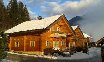 A traditional wooden house with a snow-covered roof. In the background, mountains and forests can be seen.