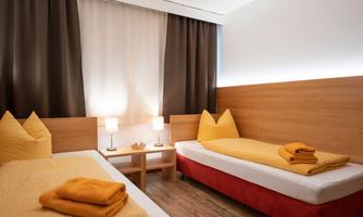 A cozy room with two single beds, decorated in warm shades of yellow. A small table with lamps and fresh towels complements the inviting atmosphere.