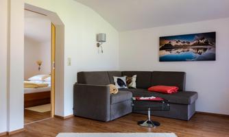 A cozy living room with a gray sofa and a table. A picture of a mountain landscape hangs on the wall.