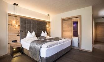 A modern bedroom with a large double bed and wooden details. The soft lighting creates a cozy atmosphere.