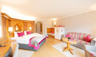 A cozy hotel room with bright wooden interiors and modern furnishings. There is a double bed, a seating area, and large windows that provide plenty of light.