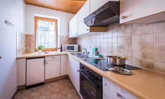 A modern kitchen with a wooden ceiling and bright walls. It includes a stove, a microwave, and a sink, as well as some kitchen utensils.