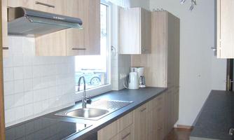A modern kitchen with wooden cabinets and a large window. The equipment includes a stove, a sink, and a refrigerator.