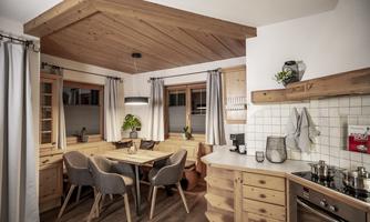 A modern kitchen with wooden shelves and a large dining table. The atmosphere is cozy and inviting.