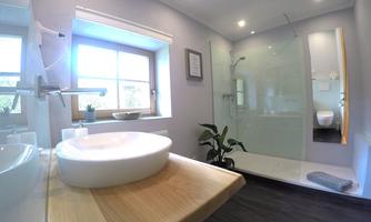 A modern bathroom with a large shower and a beautiful sink on a wooden shelf. Bright walls and a window provide plenty of natural light.
