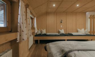 A cozy room with wooden walls and a modern, simple design. There are seating areas with cushions and windows that let in plenty of light.