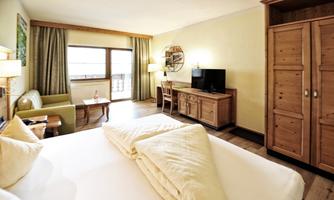 A modern hotel room with a large bed, a cozy seating area, and a TV. The walls are painted in light colors and there is plenty of natural light coming through the window.