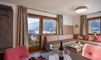 A modern living room with a cozy couch and dining table. Through large windows, you can see the mountains and nature outside.