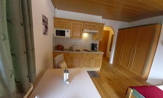 A bright and cozy kitchenette with wooden cabinets and a dining table. The space is inviting and has a modern, friendly style.