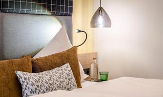A cozy bedroom with a large bed and decorative pillows. A modern light fixture and soft colors create a relaxed atmosphere.