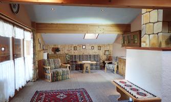 A cozy living space with wood paneling and a large window. The furnishings consist of comfortable furniture and a colorful rug.