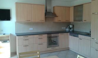 A modern kitchen with light wooden furniture and a stove. On the worktop, there is a coffee machine and other kitchen appliances.