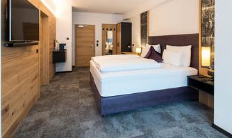 A modern hotel room with two beds and cozy furnishings. The walls are painted in light tones and wooden elements create a warm atmosphere.