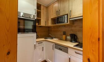 A modern kitchen with wooden shelves and white cabinets. The equipment includes a stove, a microwave, and a sink.